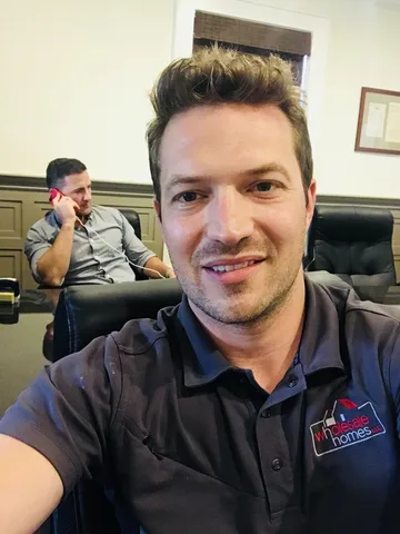 Bruce Elia Jr. taking a selfie in the office while a colleague works a deal on the phone