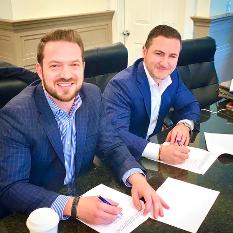 Bruce Elia Jr. and a client smiling as they sign closing paperwork at the office