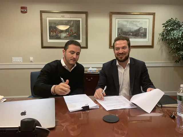 Bruce Elia Jr. signing a real estate agreement with a client at a conference table